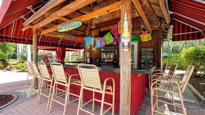 Uma área de bar com cadeiras de madeira e um balcão vermelho, decorada com bandeirinhas coloridas.