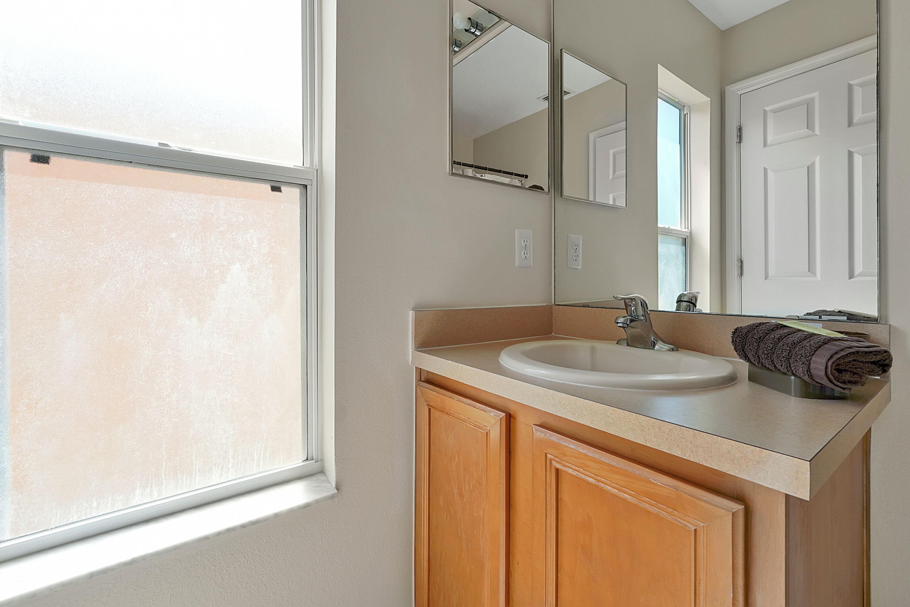 Une salle de bain avec une fenêtre, un lavabo, un miroir et des meubles en bois.