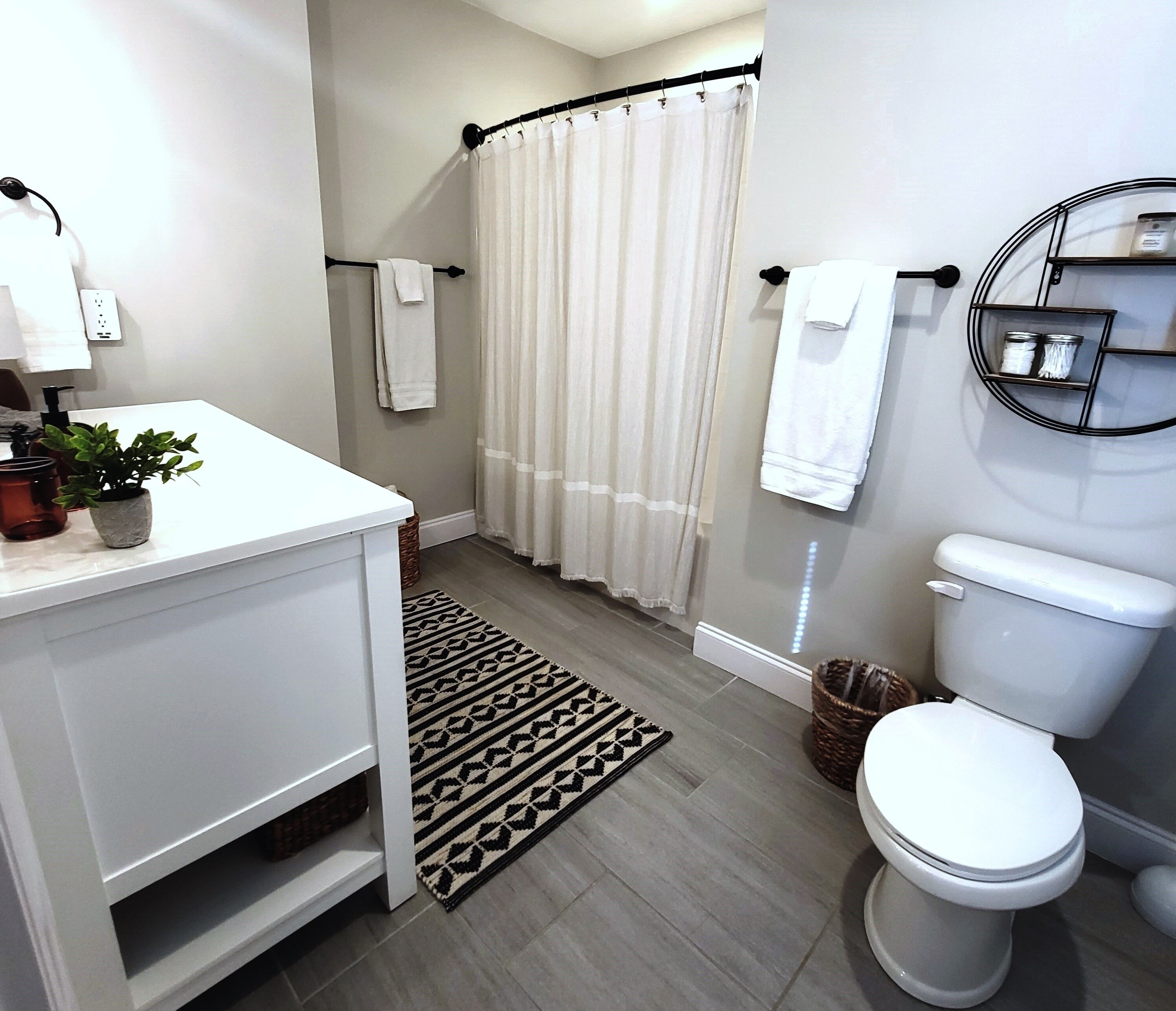Un bany modern amb un lavabo blanc, una dutxa amb cortina blanca, un vàter i una catifa amb un disseny decoratiu.