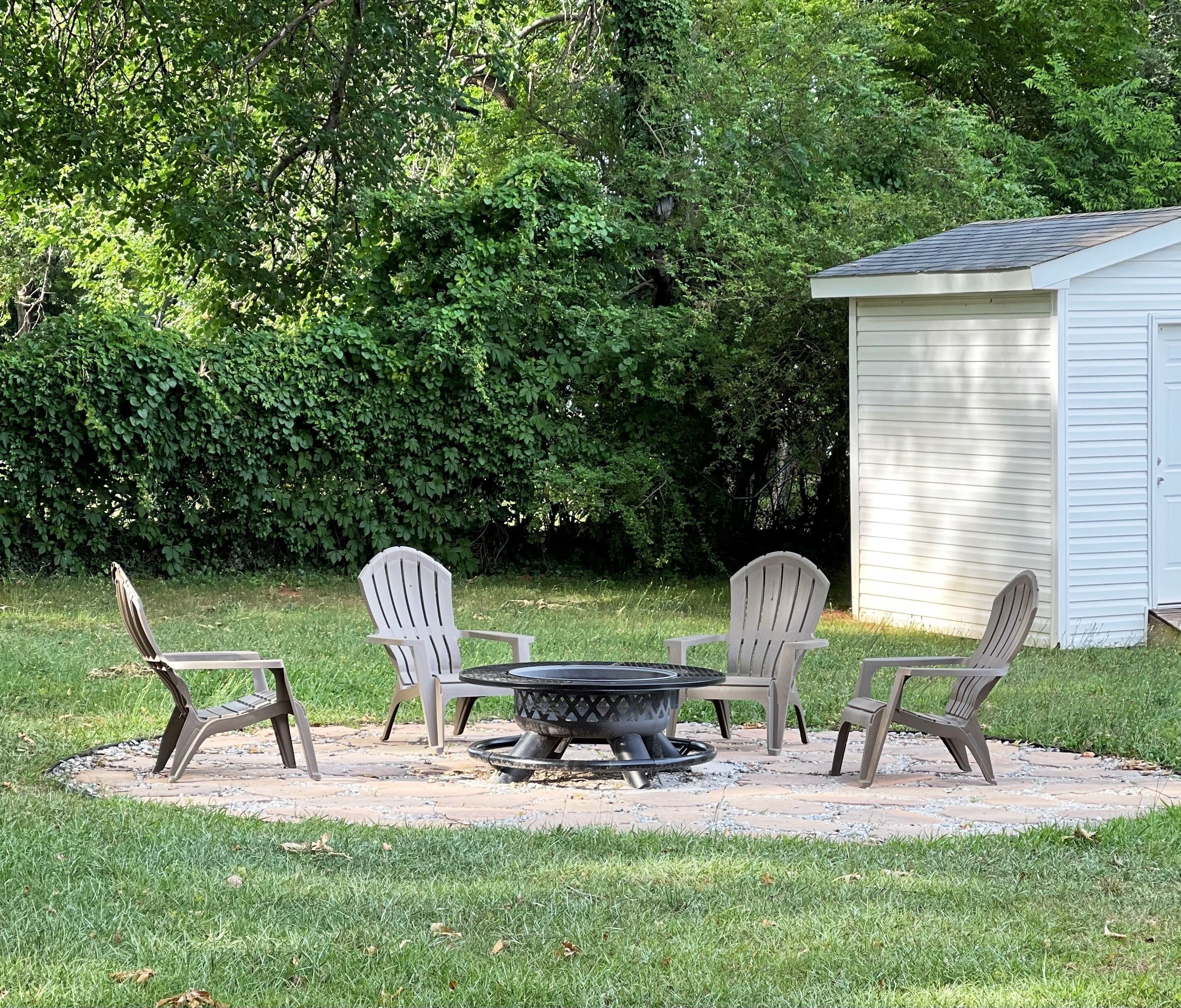 Een terras met vier Adirondack stoelen, een ronde tafel en een vuurkorf.