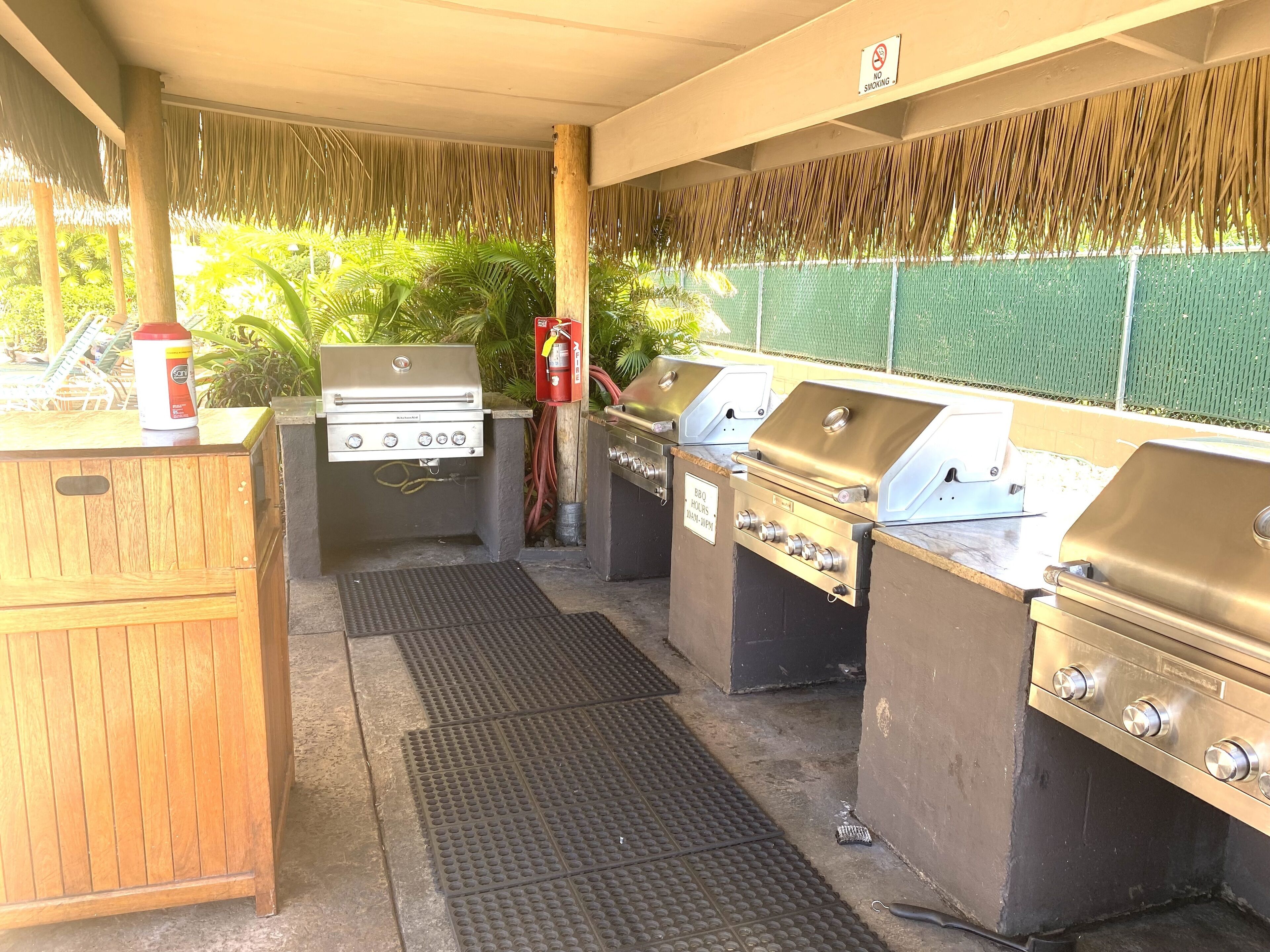 An outdoor barbecue area with multiple grills, a fire extinguisher, and a wooden cabinet.