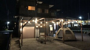 Un'area esterna coperta con una tenda, tavoli e sedie, collegata a un edificio con un balcone.