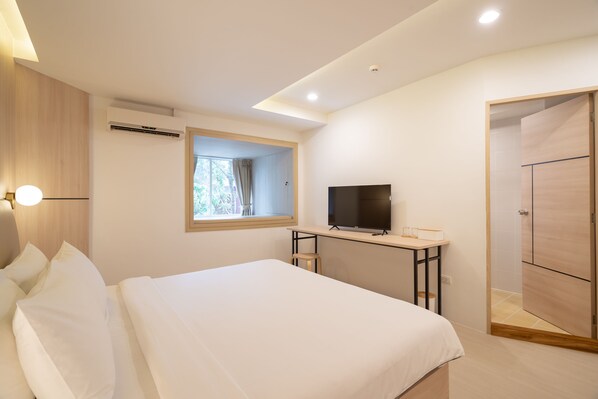 A modern hotel room with a large bed, a desk with a TV, and a wardrobe.