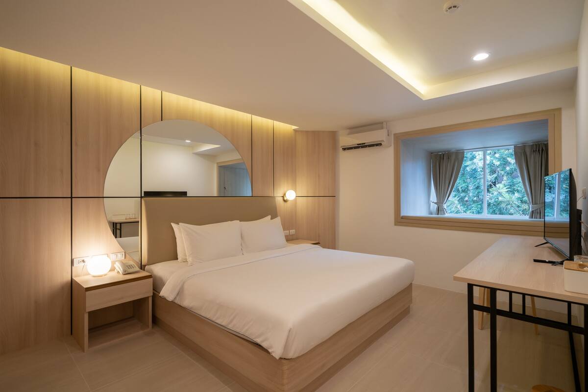 A modern bedroom with a large bed, bedside tables, a desk, and a window with curtains.