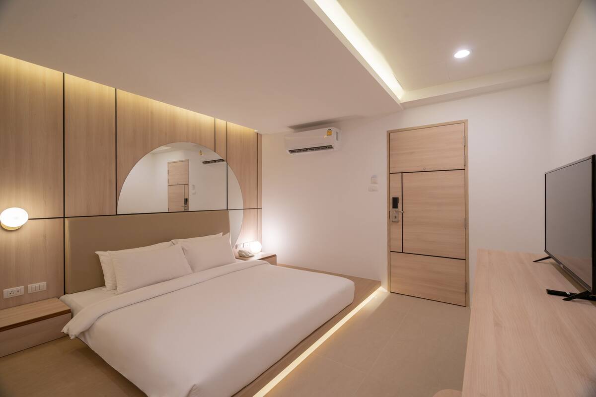 A modern bedroom with a bed, bedside table, mirror, and built-in wardrobe.