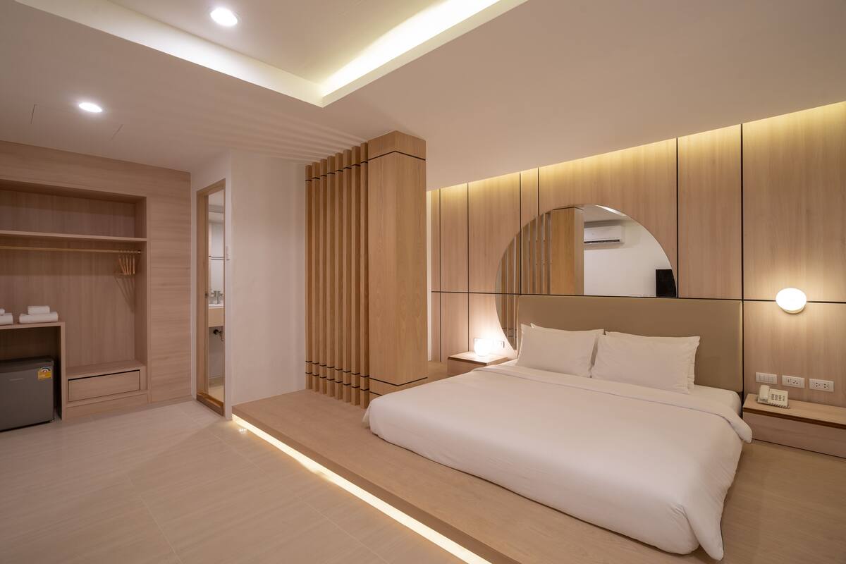 A modern hotel room with a large bed, built-in wardrobe, and a bedside table with a lamp.