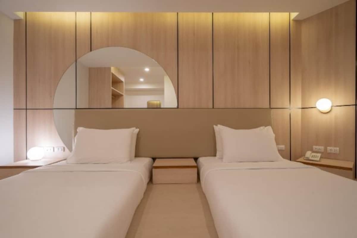 A hotel room with two beds, a large mirror, and a bedside table with a lamp.