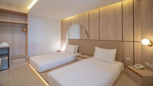 Una habitación de hotel moderna con dos camas individuales, un armario empotrado, una mesita de noche con lámpara y un espejo sobre la cama.
