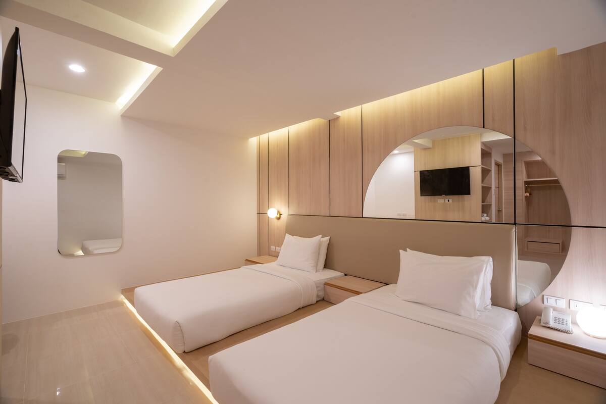 A modern hotel room with two beds, a large mirror, a flat-screen TV, and a bedside table with a phone.