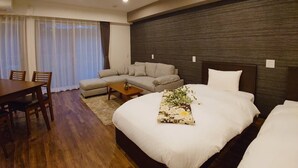 A modern hotel room with a wooden dining table, a sofa, a bed with a floral arrangement, and a dark textured wall. - Vacation Rent Kanazawa (Kanazawa)