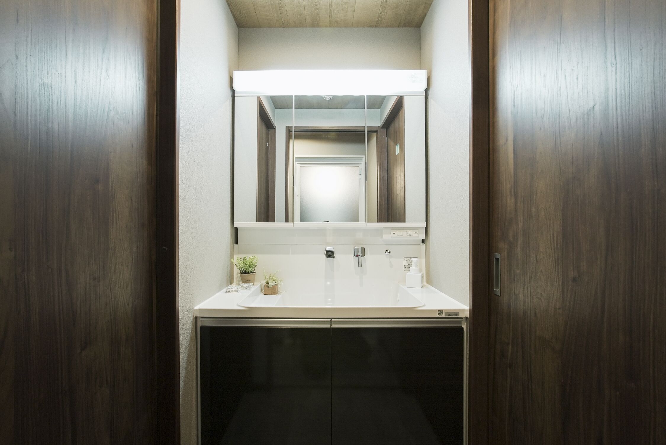A modern bathroom with a white sink, two faucets, a mirror, and a dark cabinet.