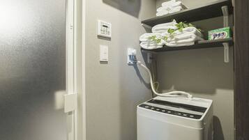 A bathroom with a white towel warmer, a wall-mounted heater, and a shelf with folded towels and a box of laundry detergent.