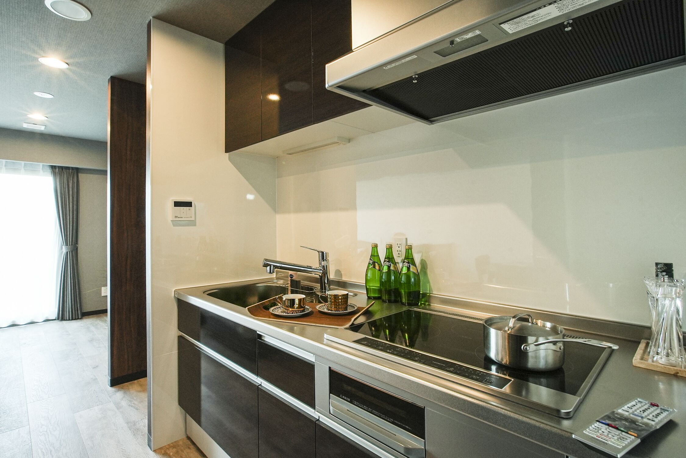 A modern kitchen with a built-in stove, a sink, and a microwave. There are green bottles on the counter and a pot on the stove.