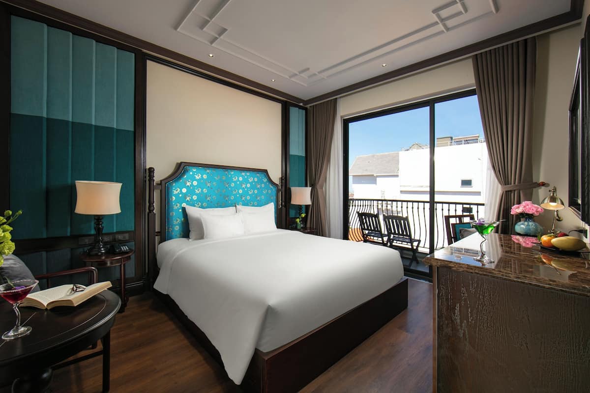 Ein Hotelzimmer mit einem großen Bett, einem Schreibtisch mit Lampe, einem Sessel und Blick ins Freie.