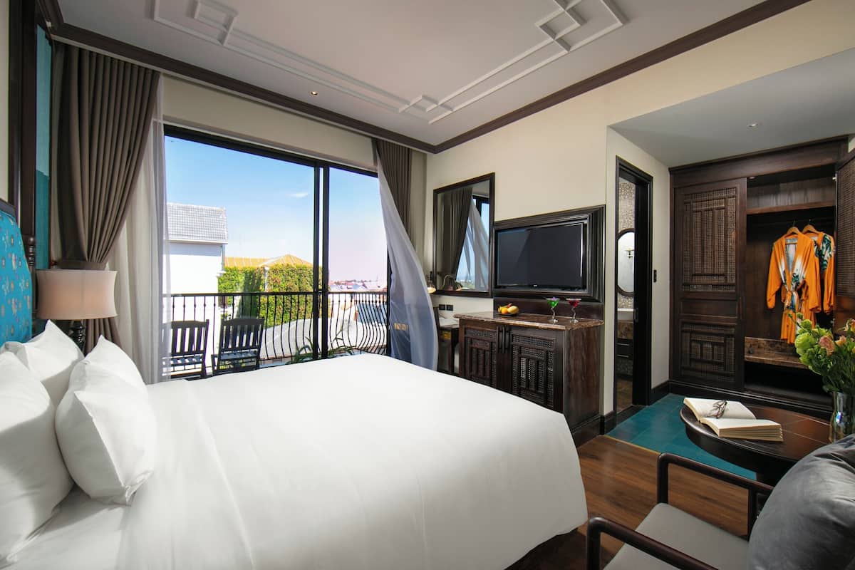 Ein Hotelzimmer mit einem großen Bett, einem Fernseher, einem Schreibtisch mit einem Laptop und Blick ins Freie.