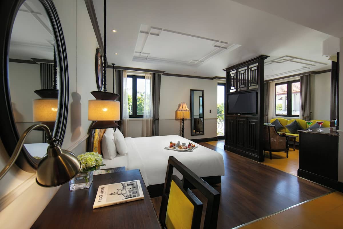 Ein Hotelzimmer mit einem großen Bett, einem Schreibtisch mit Lampe, einem Fernseher und einem Sofa.