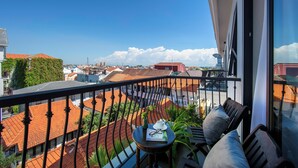 A balcony with a view of red-tiled roofs, a table with a book and glasses, and a chair with cushions. - Silkian Hoian Boutique Hotel & Spa (Da Nang)