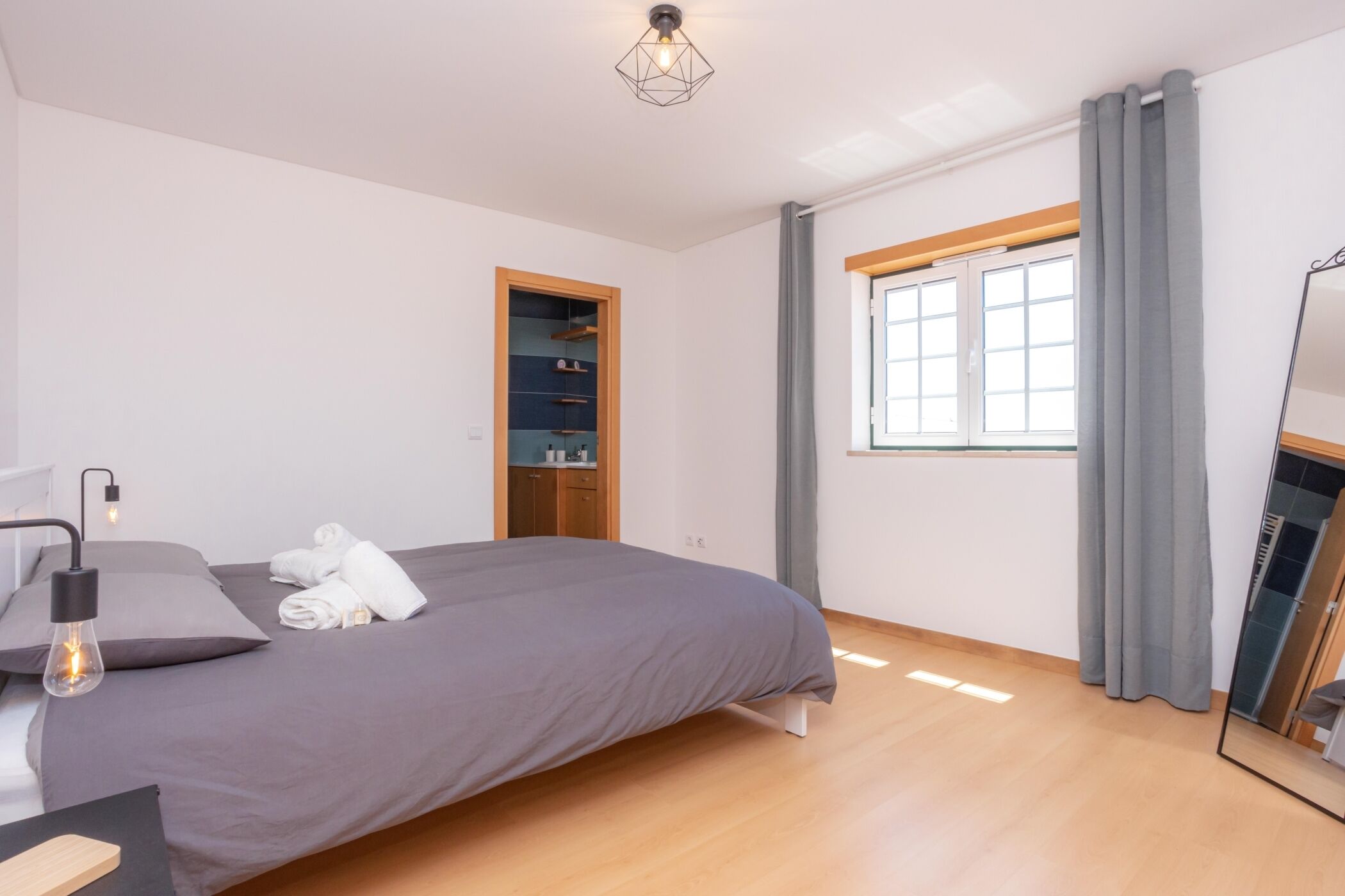 Een moderne slaapkamer met een bed, een kledingkast, een raam met gordijnen en een plafondlamp.