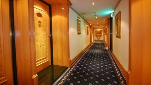 A hotel hallway with wooden doors, a patterned carpet, and framed pictures on the walls. - Karohotel (Kaohsiung)