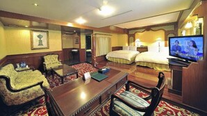 A hotel room with a wooden desk, two chairs, a bed, a television, and a small table with a book and water bottles. - Karohotel (Kaohsiung)