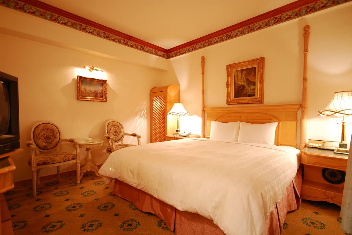 Ein Hotelzimmer mit einem großen Bett, zwei Sesseln, einem Schreibtisch, einer Lampe und einem Gemälde an der Wand.