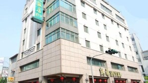 A multi-story hotel with a prominent green sign on the left side, a large entrance with red lanterns, and a traffic light above the entrance. - Karohotel (Kaohsiung)