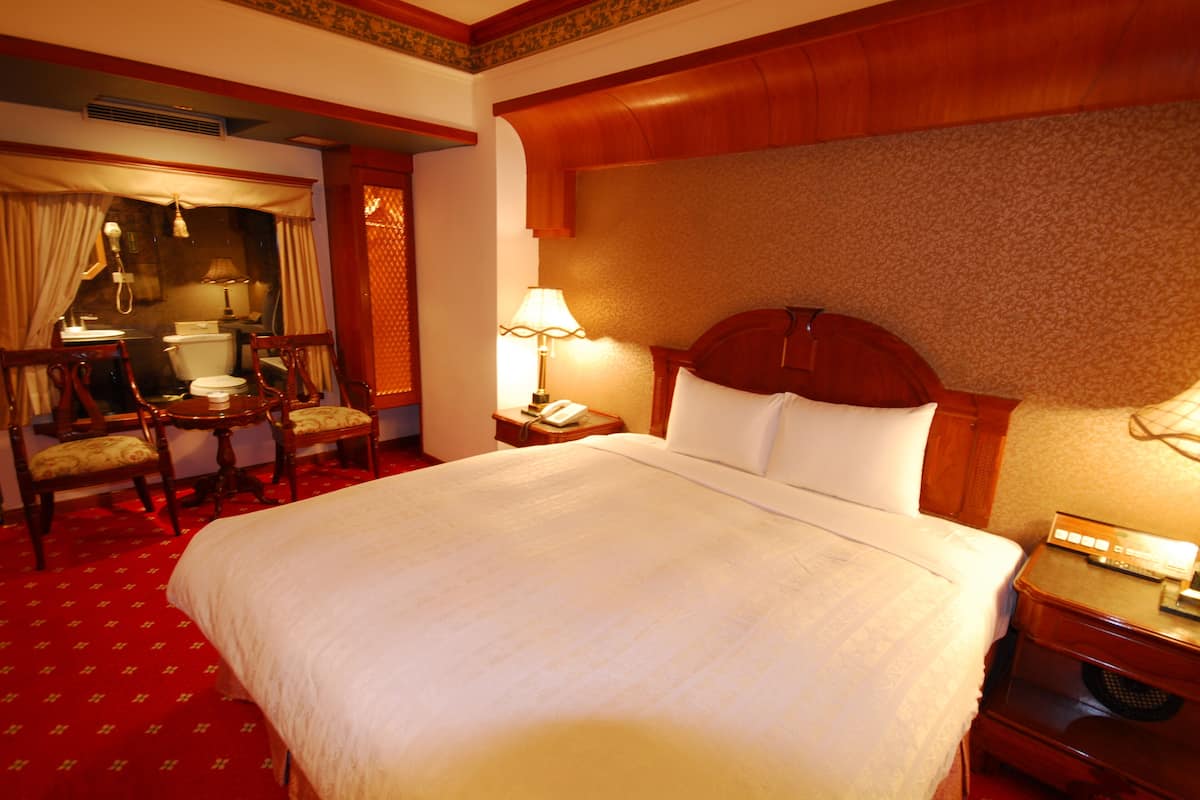 Ein Hotelzimmer mit einem großen Bett, einem Schreibtisch mit Lampe, einem Sessel, einem kleinen Tisch und einem Telefon.