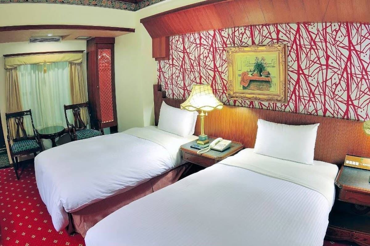 Ein Hotelzimmer mit zwei Betten, einem Schreibtisch mit Telefon, einer Lampe und einem gerahmten Bild an der Wand.