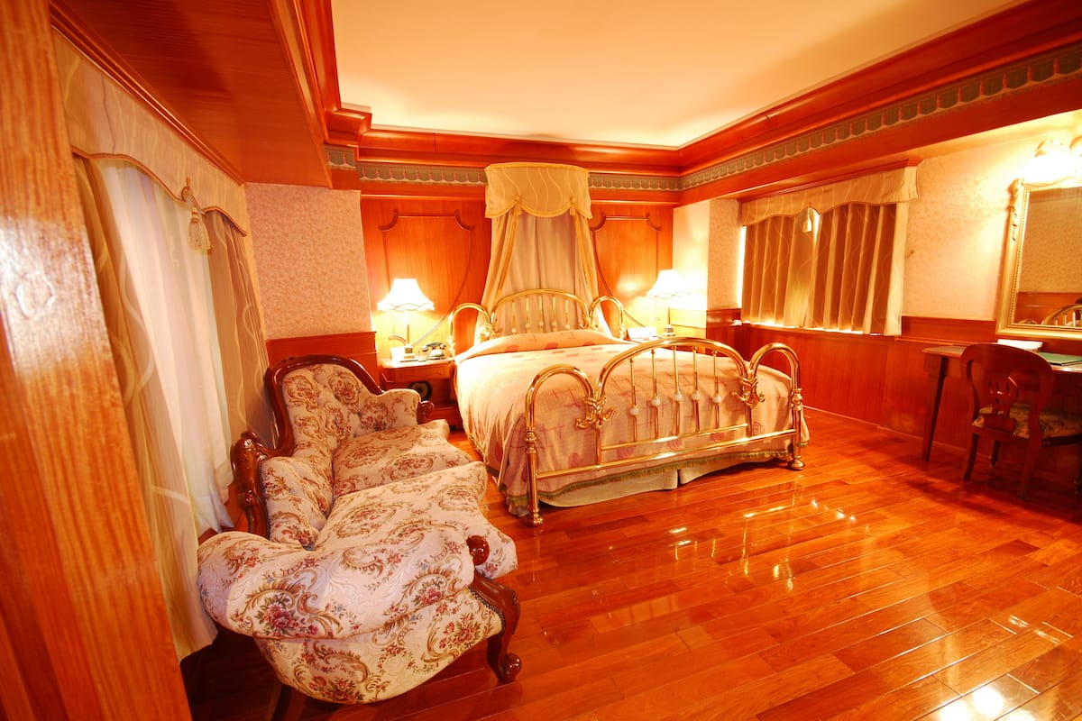 Ein klassisches Himmelbett mit Baldachin, ein Sitzsessel mit Blumenmuster und ein Holzboden.
