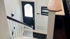 A staircase with a white railing, a black door with a glass window, and a wall-mounted clock. - NEW! Steps to DE Bay BEACH & Parks, Short Ride Cape May, Wildwood, Stone Harbor! (Cape May Beach)