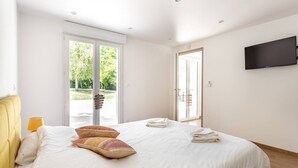 Ein Schlafzimmer mit Bett, Kissen, Fernseher und einer Schiebetür zum Balkon.