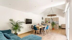 Ein modernes Wohnzimmer mit einer Sofagarnitur, einem Essbereich mit Stühlen und einem Tisch, einer Küche mit Holzschränken und einem großen Fenster.