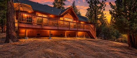 A large wooden cabin with a balcony, surrounded by trees.