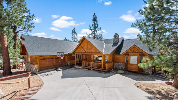 A log cabin with a stone chimney, a basketball hoop, and a porch with a railing. - Kubo Del Sol - Log Cabin, Hot Tub, Game Room, Pool Table, Ping Pong (Big Bear Lake)