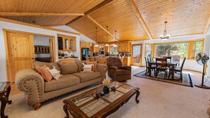 A spacious living room with a wooden ceiling, a dining area with a table and chairs, and a kitchen in the background. - Kubo Del Sol - Log Cabin, Hot Tub, Game Room, Pool Table, Ping Pong (Big Bear Lake)