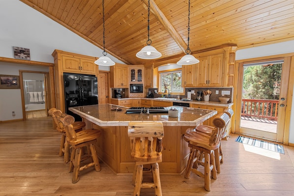 Une cuisine spacieuse avec des meubles en bois, un grand îlot central doté de tabourets et un éclairage suspendu.