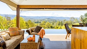 Eine Holzterrasse mit einem Korbssessel und Sesseln, mit Blick auf eine malerische Landschaft mit Hügeln und einem See.