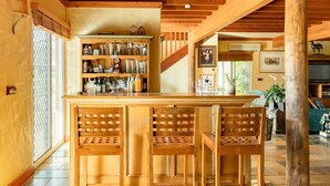 Eine Holztresore mit Flaschen und Gläsern, zwei Holzsessel und eine Holzzielende mit freiliegenden Balken.