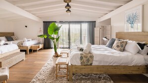 A spacious bedroom with a large bed, two smaller beds, a potted plant, and a wooden ceiling.