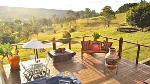 A wooden deck with a hot tub, outdoor seating, and a view of a hilly landscape.