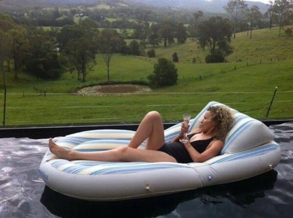 Une personne se détend sur un matelas gonflable dans une piscine, avec une vue panoramique sur un paysage verdoyant.