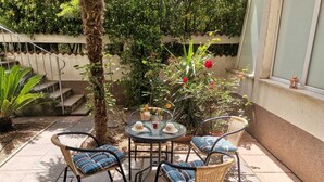 Eine Terrasse mit einem runden Tisch und vier Korbstühlen, umgeben von Topfpflanzen und einer kleinen Treppe.