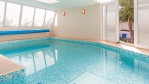 Ein Innenpool mit großen Glaswänden, gefliestem Boden und einer Sitzbank an der Wand.