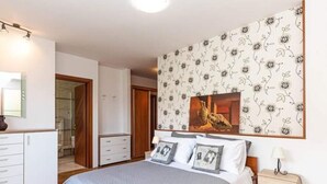 Ein Schlafzimmer mit einem Bett, einem Schminktisch, einem Nachttisch und einer Wand mit floralem Wandpapier.