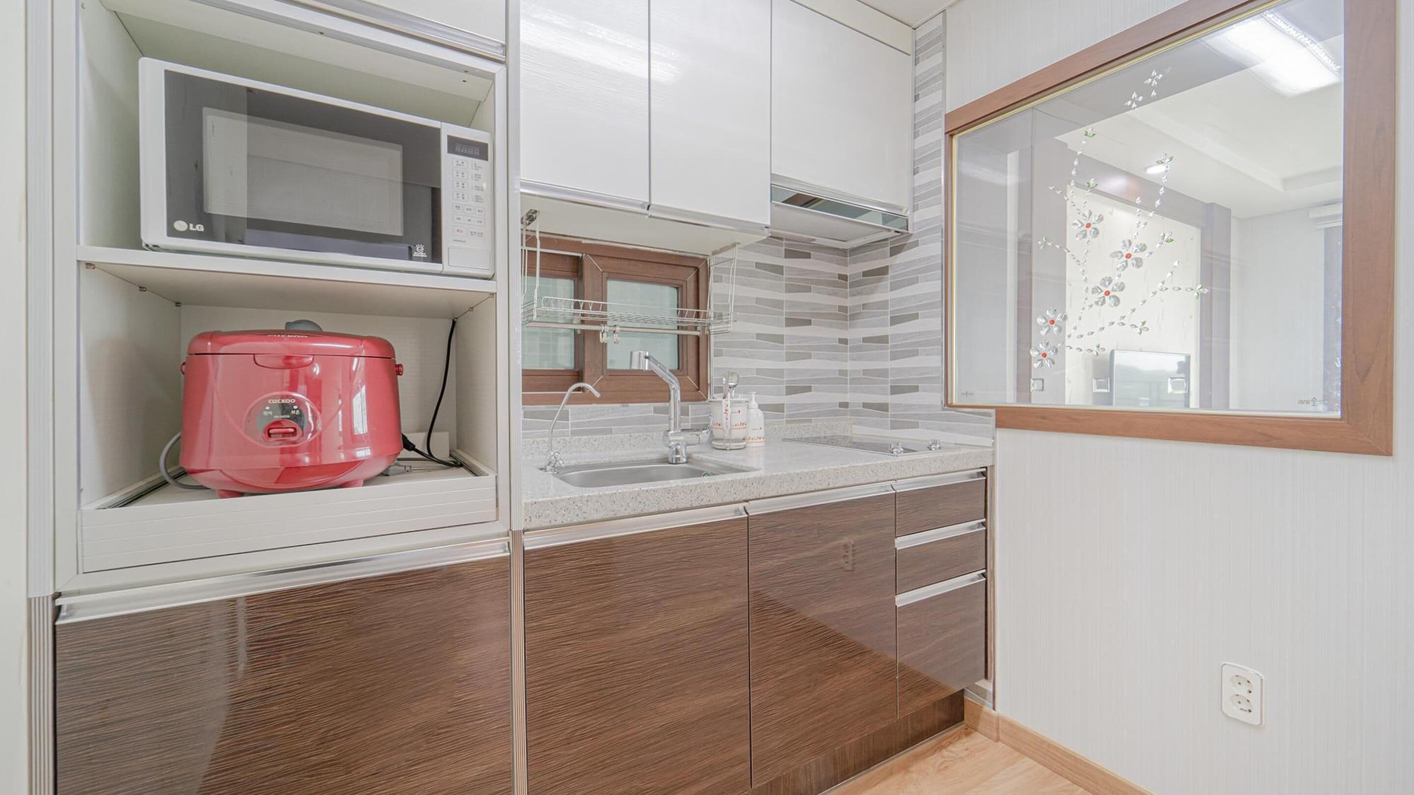 A compact kitchen with a microwave, a red appliance, and a sink.