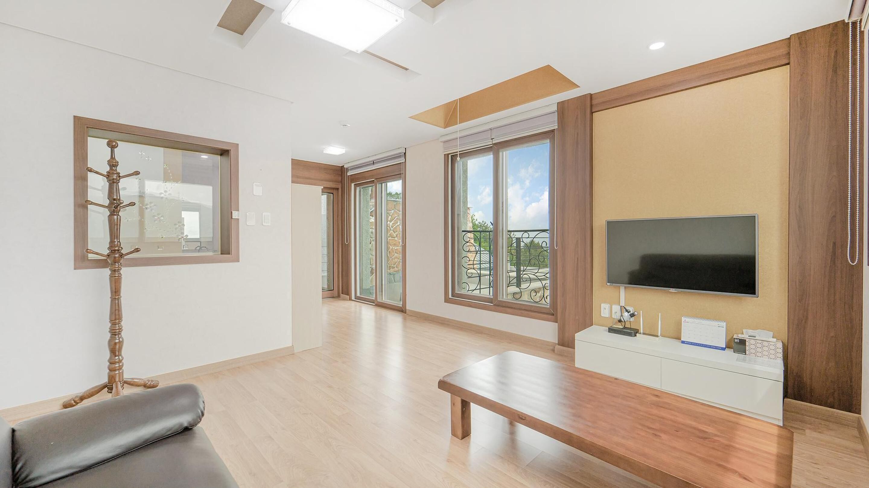 A modern living room with a large TV, wooden flooring, and a balcony view.