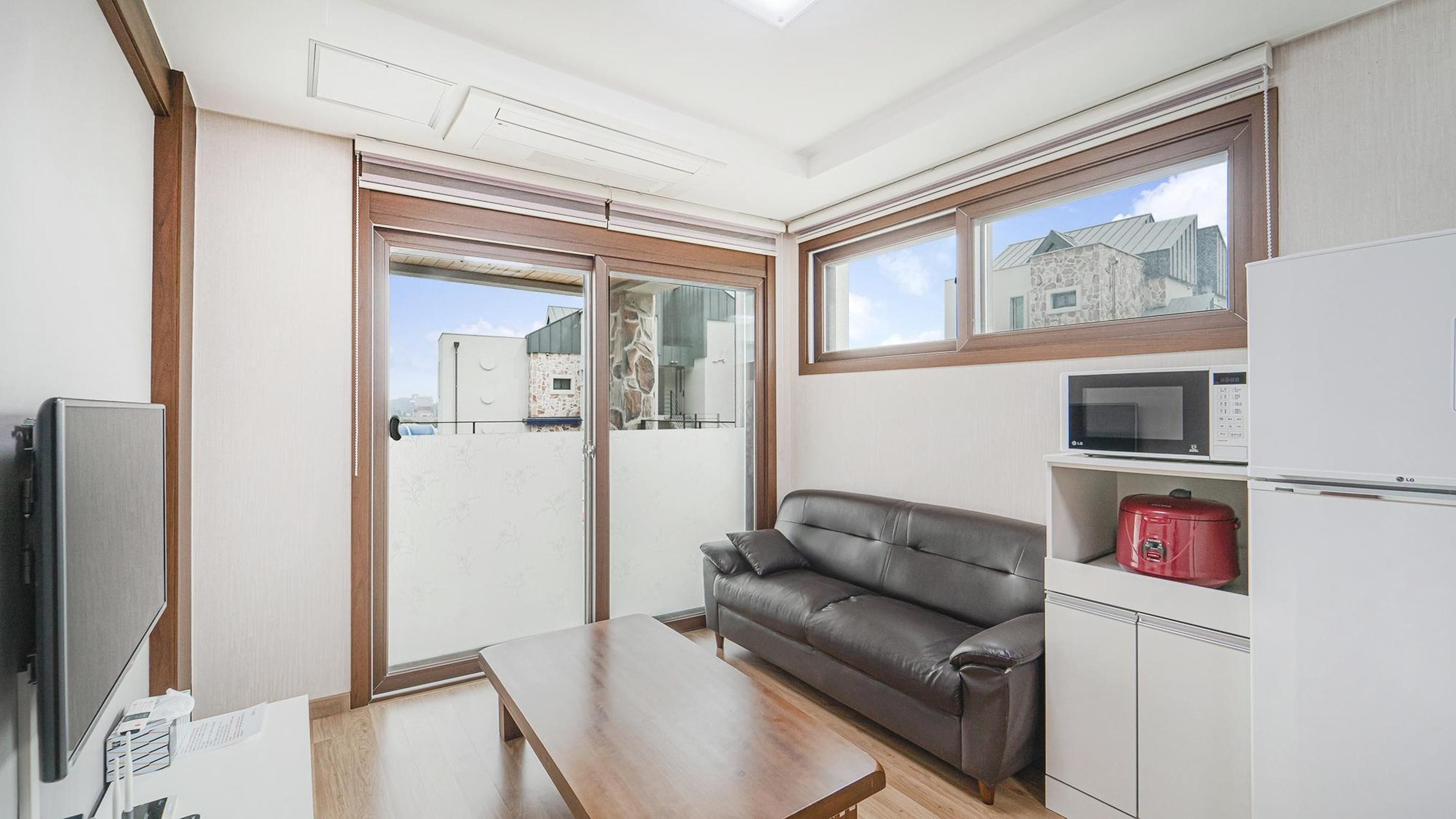 Ein kompakter Wohnraum mit einer Glastür zum Balkon, einer Couch, einem Fernseher und einer Mikrowelle.