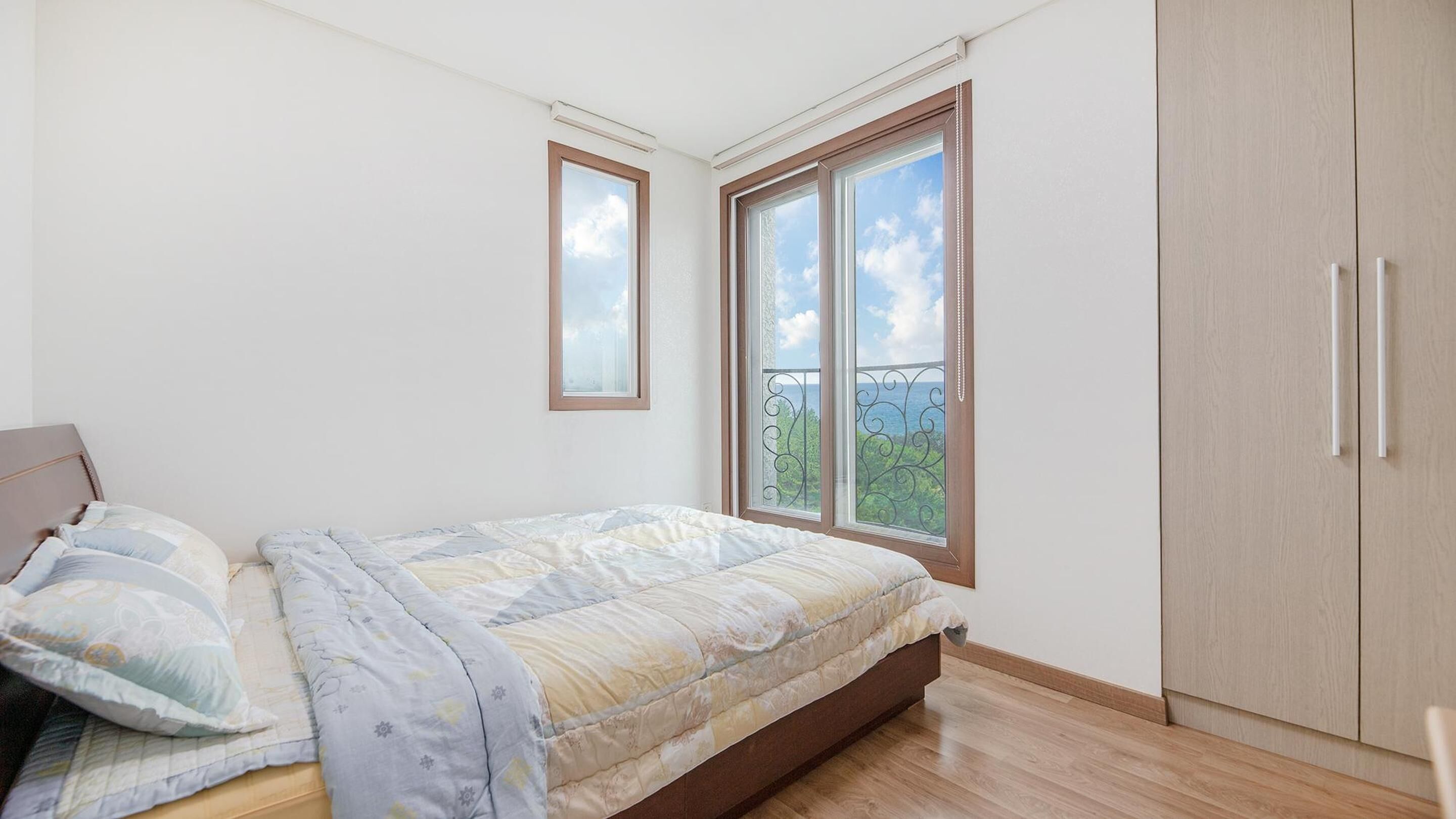 Ein Schlafzimmer mit Bett, Kleiderschrank und Fenster mit Blick ins Grüne.