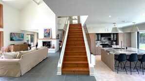 Amplia sala de estar con una escalera de madera que conduce a una cocina y comedor.