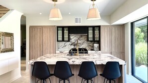 Una cocina moderna con una isla de mármol, taburetes negros y lámparas colgantes.